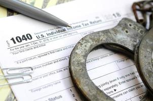 Police handcuffs lie on the tax form 1040. The concept of problems with the law in the aftermath of non-payment of taxes photo