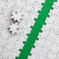 The green path is laid on the platform of a white folded jigsaw puzzle. The missing elements of the puzzle are stacked nearby. Texture image with space for text photo