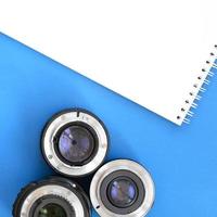 Several photographic lenses and white notebook lie on a bright blue background. Space for text photo