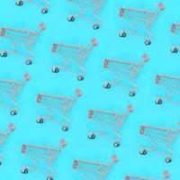 Shopping addiction, shopping lover or shopaholic concept. Many small empty shopping carts perform a pattern on a pastel colored paper background. Flat lay composition, top view photo