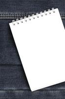 White notebook with clean pages lying on dark blue jeans background. Image with copy space photo