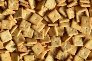 A lot of small cookies are square shaped. A pattern of a yellow salt cracker. Background image with salted pastry photo