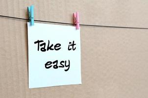 Take it easy. Note is written on a white sticker that hangs with a clothespin on a rope on a background of brown cardboard photo