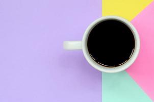 Small white coffee cup on texture background of fashion pastel blue, yellow, violet and pink colors paper in minimal concept photo