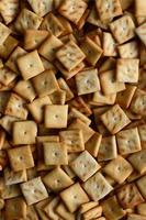 A lot of small cookies are square shaped. A pattern of a yellow salt cracker. Background image with salted pastry photo