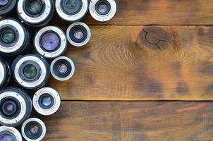 Several photographic lenses lie on a brown wooden background. Space for text photo