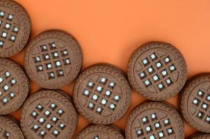 Detailed picture of dark brown round sandwich cookies with coconut filling on an orange surface. Background image of a close-up of several treats for tea photo