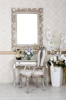 A fragment of a retro interior with a chair and table, on which is a telephone and a vase of flowers. Above the table hangs an empty picture frame for your photo