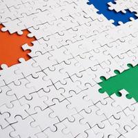 Close-up texture of a white jigsaw puzzle in assembled condition with missing elements, under which surfaces of different colors photo