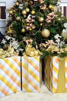 foto de cajas de regalo de lujo bajo el árbol de navidad, decoraciones caseras de año nuevo, envoltorio dorado de regalos de santa, abeto festivo decorado con guirnaldas, adornos y juguetes, celebración tradicional