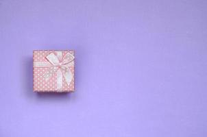 Small pink gift box lie on texture background of fashion pastel violet color paper in minimal concept photo