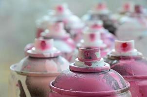 A lot of dirty and used aerosol cans of bright pink paint. Macro photograph with shallow depth of field. Selective focus on the spray nozzle photo