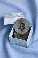 el bitcoin plateado se encuentra en una pequeña caja de regalo azul con un pequeño lazo sobre una manta hecha de tela suave y esponjosa de color azul claro con una gran cantidad de pliegues en relieve foto