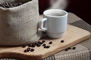 una bolsa llena de granos de café marrones y una taza blanca de café caliente l foto