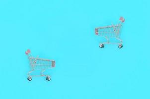 Shopping addiction, shopping lover or shopaholic concept. Small empty shopping cart lies on a pastel colored paper background. Flat lay minimal composition, top view photo