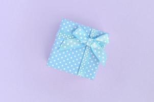 Small blue gift box with ribbon lies on a violet background. Minimalism flat lay top view photo