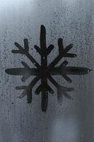 The image of the snowflake is drawn with a finger on the surface of a misted glass window. Frosty weather photo