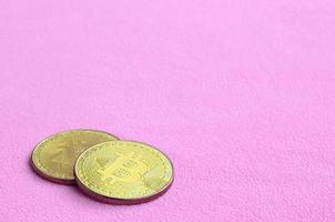 Two golden bitcoins lies on a blanket made of soft and fluffy light pink fleece fabric. Physical visualization of virtual crypto currency photo