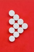 Several white tablets lie on a bright red background in the form of a triangular arrow. Background image on medicine and pharmaceutical topics photo