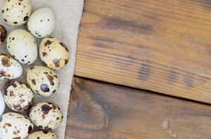 Quail eggs on sacking on a dark brown wooden surface, top view, empty place for text, recipe photo