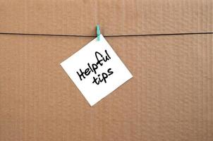 Helpful tips. Note is written on a white sticker that hangs with a clothespin on a rope on a background of brown cardboard photo