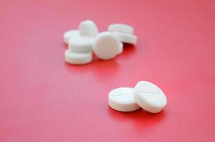 A few white tablets lie on a bright red background surface. Background image on medical and pharmaceutical topics photo