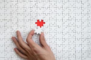 The texture of a white puzzle puzzle in the assembled state with one missing element that the male hand puts in photo