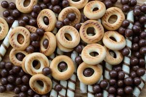 A lot of crispy sweet tubules, chocolate melting balls and yellow bagels lie on a wooden surface. Close up view photo