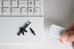 la mano inserta una tarjeta SD compacta en la ranura de la netbook, en la que se encuentran un cuchillo en miniatura y una pistola. el concepto de juegos de computadora sobre temas militares, tiradores en línea y simuladores de guerra foto