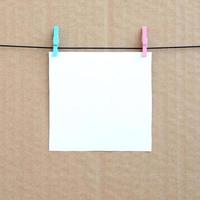 White blank card on rope on a brown cardboard background. Creative reminder, small sheet of paper on wooden clothespin, memo backdrop photo