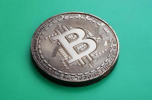 Chocolate product in the form of physical bitcoin lies on a green plastic background. Model of the crypto currency in the edible form photo