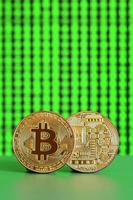 Two gold bitcoins lie on the green surface on the background of the display, which shows the process of mining the crypto currency photo