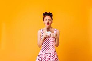 Amazed female model in polka-dot dress looking at camera. Studio shot of pinup woman with ginger ha photo