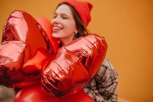 Photo of red balloons and happy young girl who received them as gift on orange background