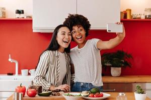 Lovely ladies in white tops pose for selfie while cooking vegetable lunch. photo