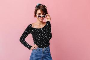 Confident girl in dotted shirt looking at camera. Studio shot of short-haired woman in sunglasses i photo