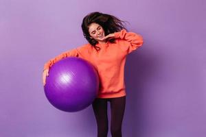 Slender lady holds huge fitball. Woman in sport outfit smiling on isolated background photo