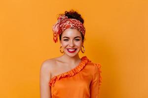 Young girl in great mood is smiling on orange background. Stylish dark-haired lady in orange blouse photo