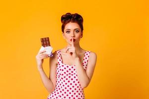 Elegant pinup young woman holding chocolate. Front view of ginger lady in polka-dot dress touching