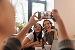 Cropped view of girl with smartphone and her laughing friends. Selective focus of photofrapher taking picture of happy women photo