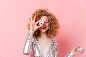 Close-up portrait of curly blonde girl with charming smile covering eye with mini disco ball on pin photo