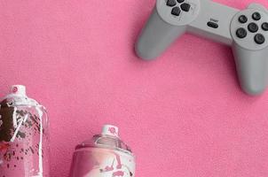 concepto de estilo de vida de adolescentes y jóvenes. joystick y dos latas de aerosol se encuentran sobre la manta de tela de lana rosa peluda. controladores para videojuegos y latas de pintura sobre un fondo de material de vellón de felpa foto