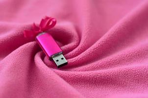 Brilliant pink usb flash memory card with a pink bow lies on a blanket of soft and furry light pink fleece fabric with a lot of relief folds. Memory storage device in women's design photo