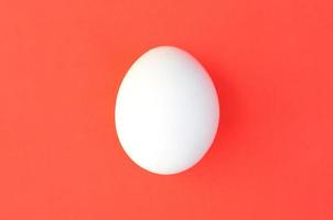 un huevo blanco sobre un fondo rojo brillante foto
