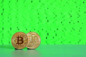 Two gold bitcoins lie on the green surface on the background of the display, which shows the process of mining the crypto currency photo