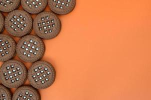 Detailed picture of dark brown round sandwich cookies with coconut filling on an orange surface. Background image of a close-up of several treats for tea photo