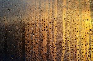 The texture of misted glass with a lot of drops and drips of condensation against the sunlight at dawn. Background image photo