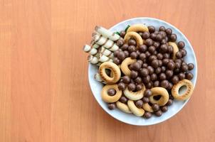 túbulos crujientes, bolas de fusión de chocolate y bagels yacen en un plato blanco sobre una mesa de madera. mezcla de varios dulces foto