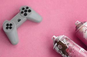 Teenagers and youth lifestyle concept. Joystick and two spray cans lies on the blanket of furry pink fleece fabric. Controllers for video games and paint cans on a plush fleece material background photo