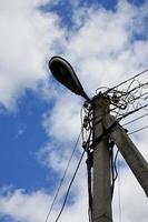 antiguo poste eléctrico de hormigón para la transmisión de electricidad por cable con poste de luz sobre un fondo de cielo azul nublado. método obsoleto de suministro de electricidad para su uso posterior foto